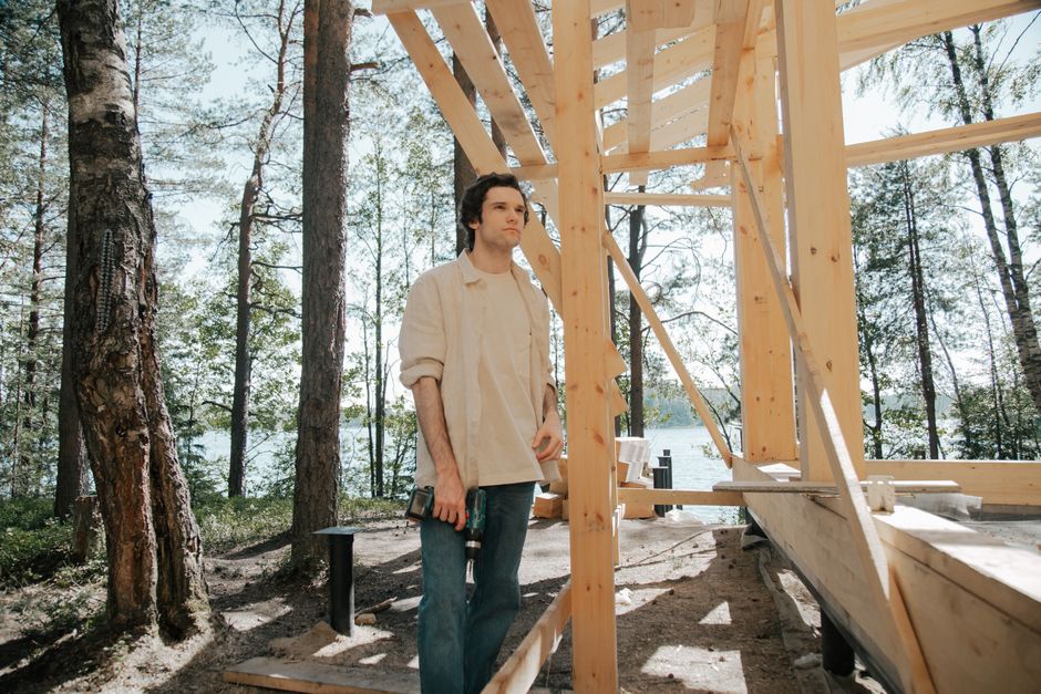 Carpenter working on wooden house frame outdoors, by a lake.