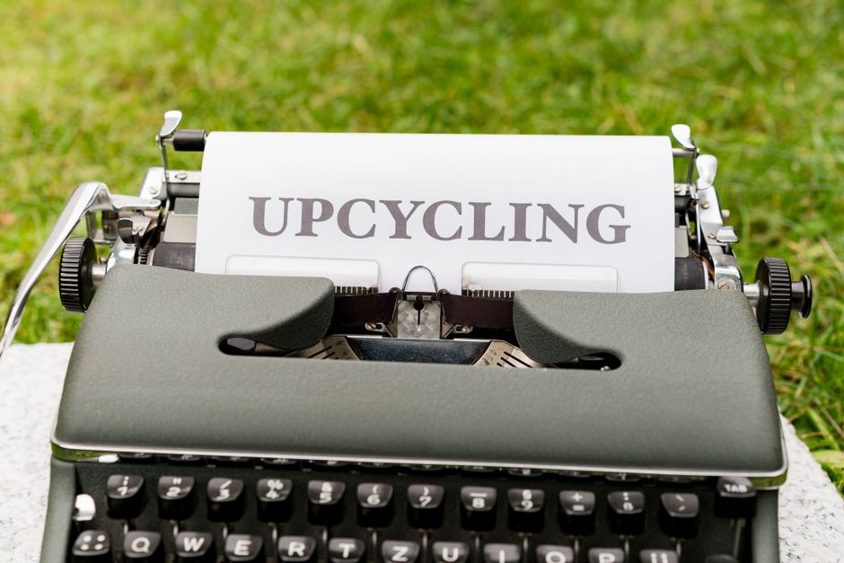 A retro typewriter displaying the word 'upcycling' outdoors on grassy ground.