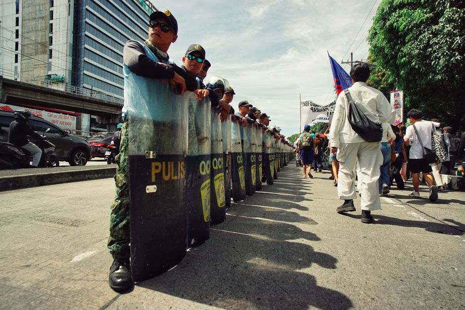 Police officers forming a line during a city protest, with demonstrators approaching.
