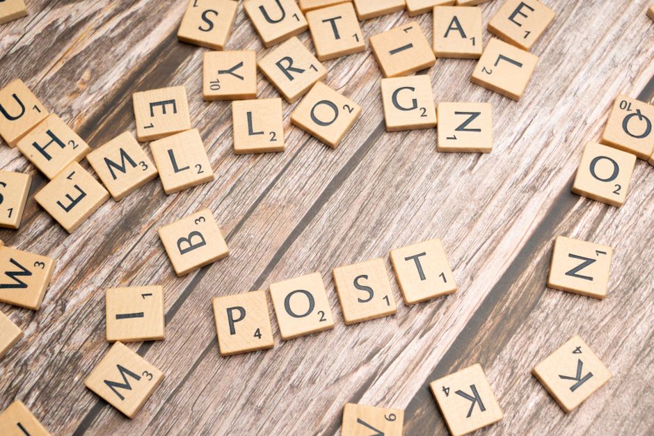 Wooden scrabble tiles scattered with the word 'POST' on a rustic wooden surface.