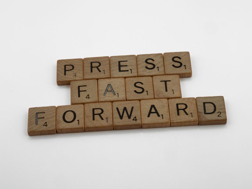 Wooden Scrabble tiles arranged to spell 'Press Fast Forward' on a white background.