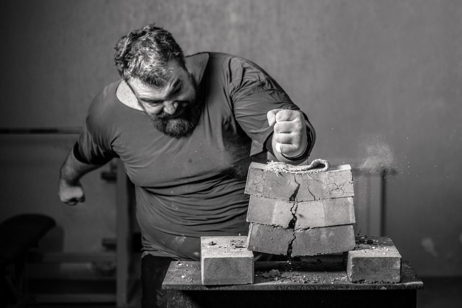 Powerful image of a man smashing bricks with his fist in a grayscale setting.