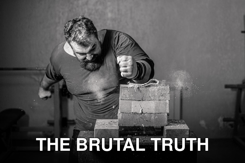 Dramatic grayscale image of a man breaking bricks indoors with powerful force.