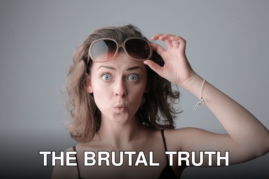 Woman with surprised expression lifting sunglasses indoors. Casual and playful mood.