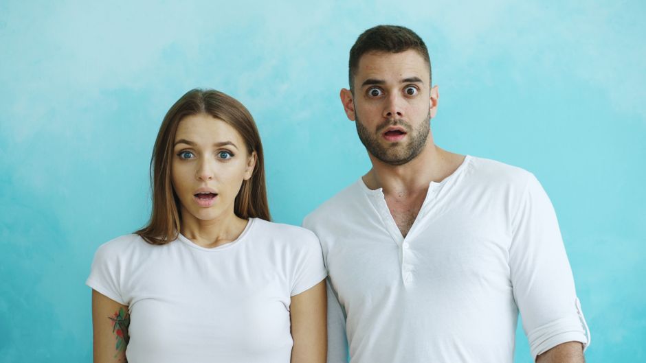 A young couple shows surprised expressions against a light blue background.
