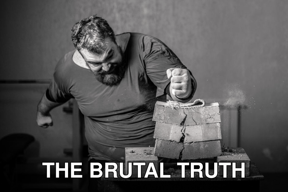 Powerful image of a man smashing bricks with his fist in a grayscale setting.