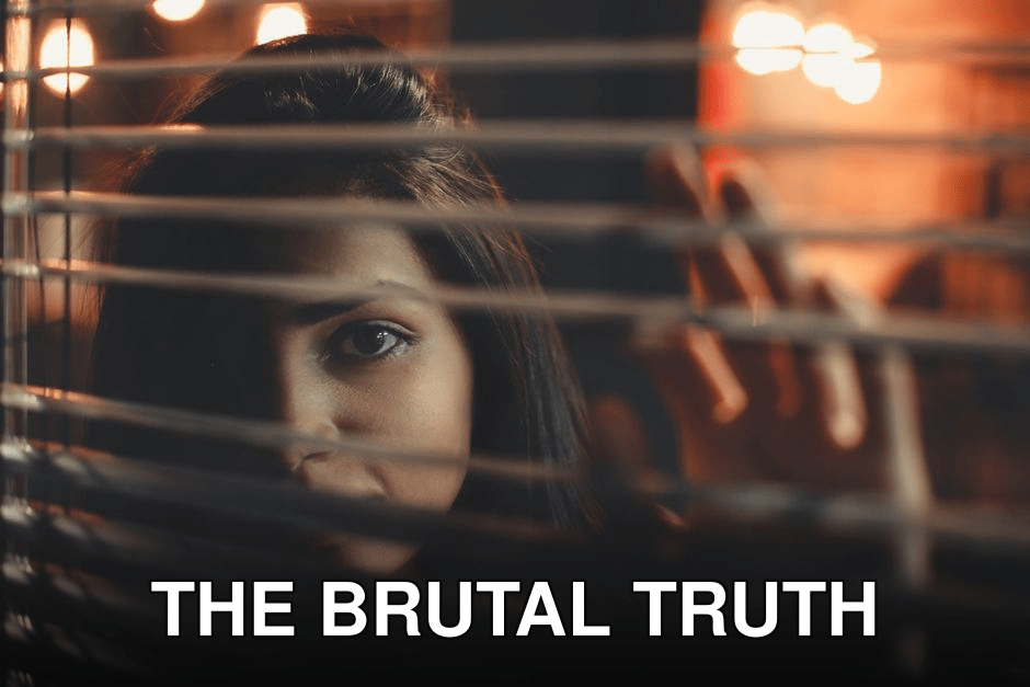 A woman peering through window blinds with a contemplative expression at night.