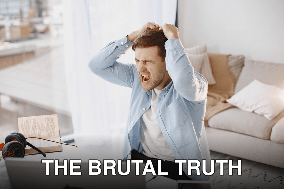 An upset man with mouth open, pulling hair at a desk with a laptop in a home setting.