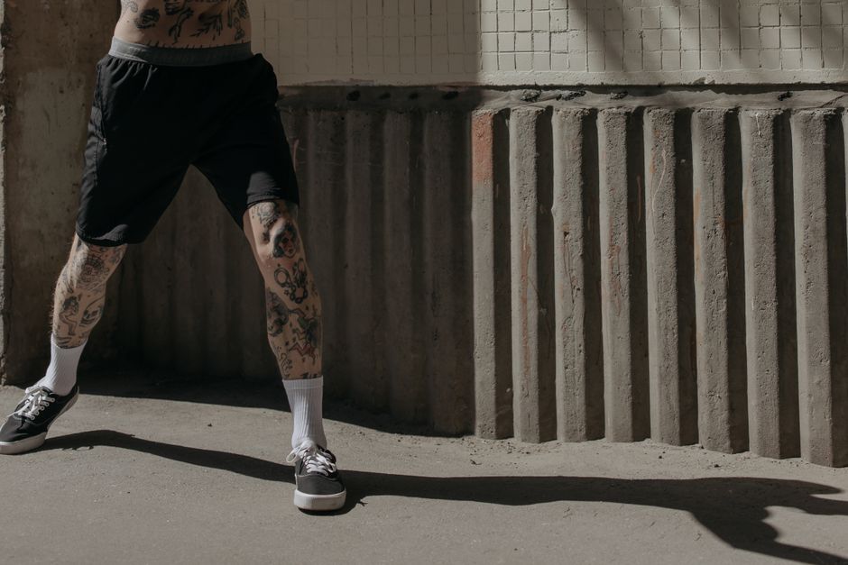 Crop unrecognizable hipster male athlete in shorts and gumshoes standing with spread legs while training on street