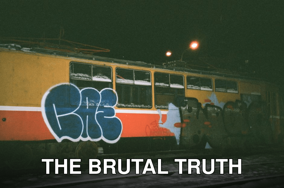 A streetcar covered in graffiti art parked on snowy railroad tracks at night.
