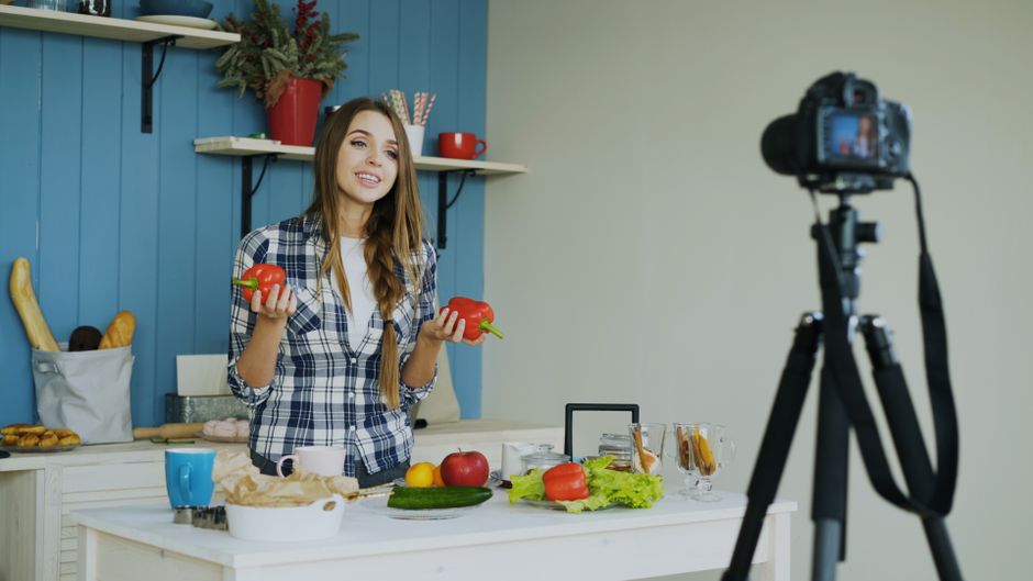 Woman filming a cooking vlog in a modern kitchen setup with fresh vegetables.