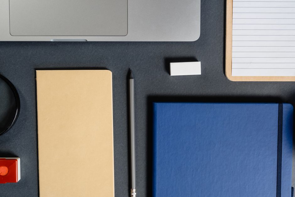 Flat lay of assorted office supplies including notebook, pencil, and laptop on a dark desk.