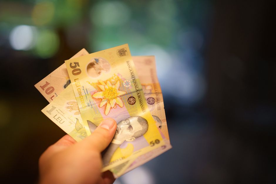 Hand holding Romanian Lei banknotes in a blurred indoor setting, highlighting currency details.