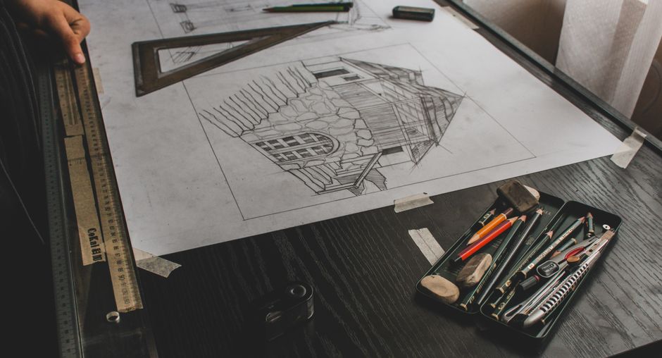 Close-up of an architectural sketch with drafting tools on a desk.