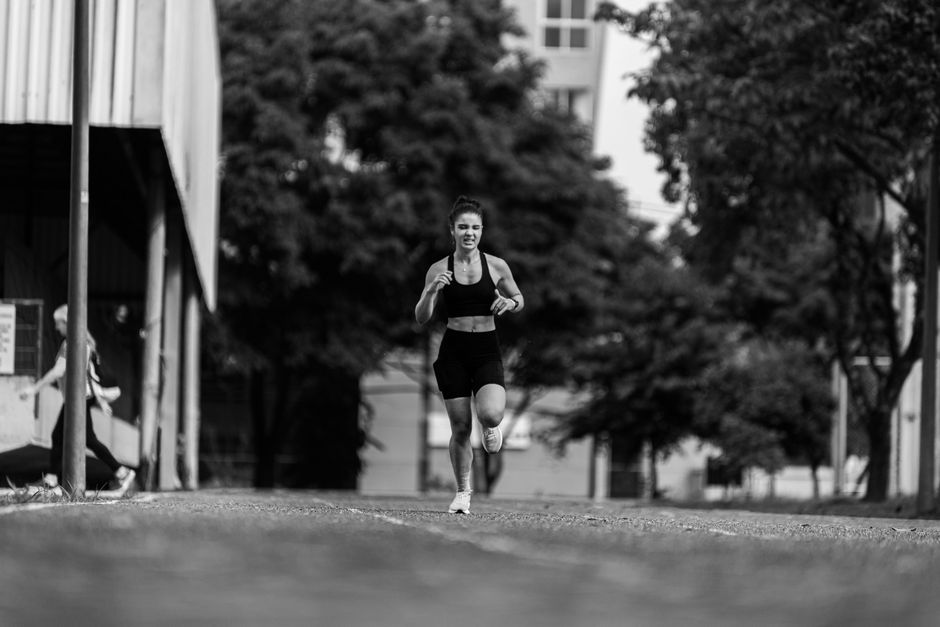 A young woman runs energetically outdoors, captured in a dynamic black and white photo.
