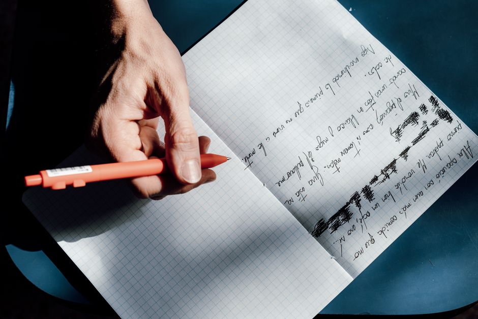 A person practicing handwriting using a red pen in a notebook during a sunny day in Buenos Aires.