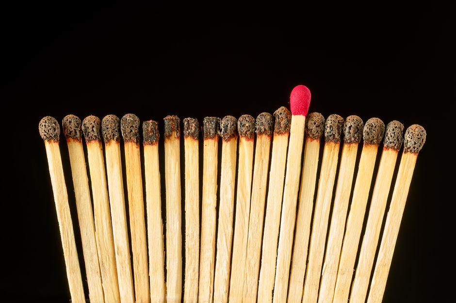A standout red-tipped match among burnt ones, symbolizing uniqueness and individuality.