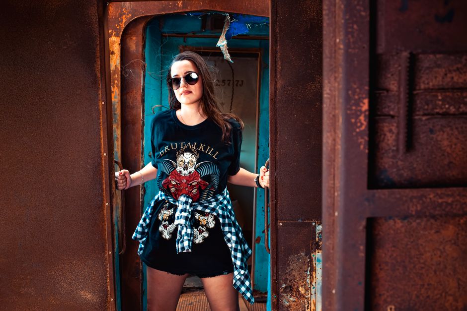 Portrait of a stylish woman in sunglasses standing in a rustic doorway with a bold graphic tee.