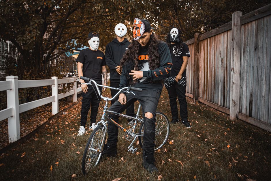Group of masked individuals posing with bicycle in a fall backyard setting.