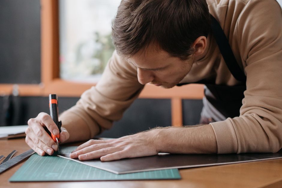 Focused man cuts material using precision knife on a wooden board in a workshop setting.